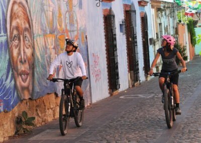 Two people riding bike while looking at street art wall