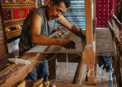 A man operates a traditional loom, weaving threads to create a textile.