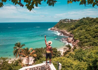A person standing on the edge of the cliff looking at the beach below