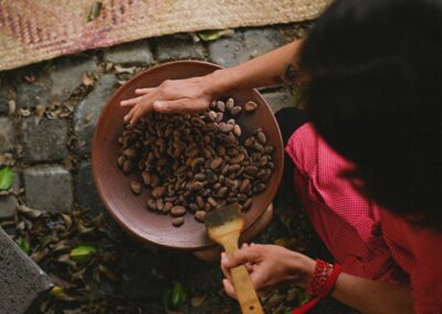 A person scooping chocolate beans with hand and a wooden spoon from pottery plate